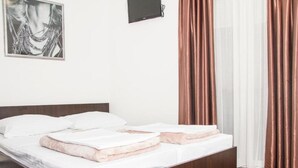 Ein ordentlich bezogenes Bett mit weißen Leinen und rosa Akzenten, ein hölzernes Kopfende, ein brauner Teppich und ein gerahmtes Bild an der Wand.