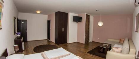A hotel room with two beds, a sofa, a TV, and a wooden floor.