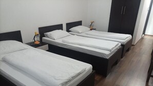 Une chambre d’hôtel avec trois lits simples, un plancher en bois et une armoire.