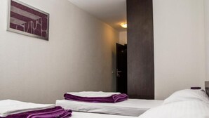 Ein Hotelzimmer mit zwei Betten, jeweils mit weißer Bettwäsche und violetten Handtüchern. An der Wand hängt ein Gemälde und in der Ecke steht eine dunkle Säule.