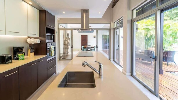 A modern kitchen with a central island, stainless steel appliances, and a view to an outdoor deck. - Casa Harmonia Modern Tropical Villa with Private Pool in Potrero (Potrero)