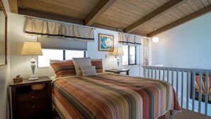Une chambre avec un grand lit, deux tables de chevet, une fenêtre avec des rideaux, un tableau au mur et un balcon avec une balustrade.