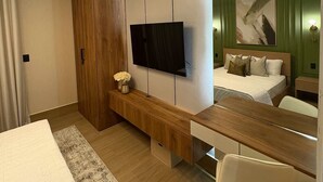 Una habitación de hotel moderna con una cama grande, un televisor montado en la pared, un mueble de madera y un escritorio con una silla.