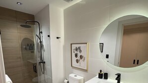 Un baño moderno con ducha envuelta en vidrio, inodoro y tocador con un espejo grande.