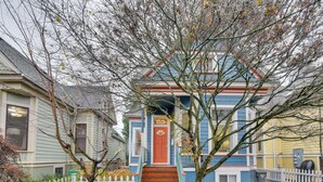 Une maison à deux étages avec une porte rouge, une clôture blanche en piquets et un arbre devant.
