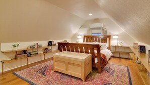 Une chambre mansardée chaleureuse, avec un lit en bois, un petit bureau et un tapis coloré.