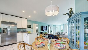 A modern kitchen with white cabinets, a stainless steel refrigerator, and a dining area with a round table and wicker chairs. - Bike to State Park: Family Getaway in Naples (Naples)