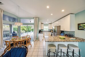 A modern kitchen with a central island, white cabinets, and a dining area with wicker chairs. - Bike to State Park: Family Getaway in Naples (Naples)