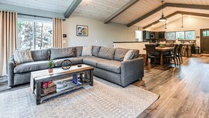 Ein modernes Wohnzimmer mit einer Eckcouch, einem Couchtisch und einem Essbereich, im Hintergrund eine Küche.