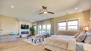 A bedroom with a large bed, a ceiling fan, a TV, a desk, and a window with curtains. - Walk to Water & Greenway! Luxe Carolina Beach Home (Carolina Beach)