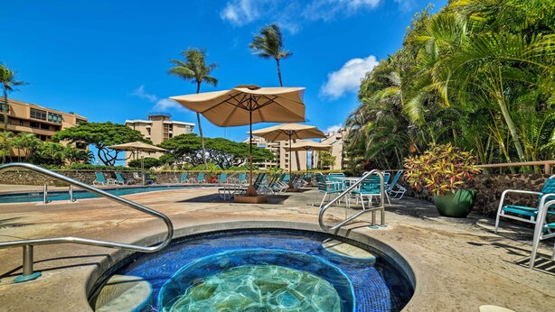A swimming pool with lounge chairs and umbrellas, surrounded by palm trees and buildings. - Walk to Beach, Pool Access! 'Kahana Coastal Condo' (Lahaina)