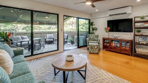 A modern living room with a sofa, a round coffee table, a TV, and a ceiling fan. - Walk to Beach, Pool Access! 'Kahana Coastal Condo' (Lahaina)