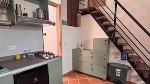 Een compacte keuken met een gasfornuis, een kleine koelkast en een vuilnisbak.