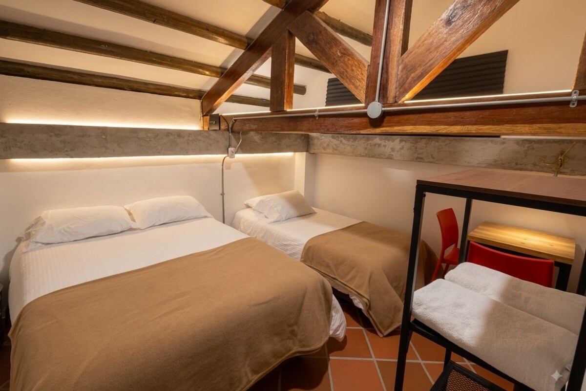 A room with two beds, a bench, and a red chair.