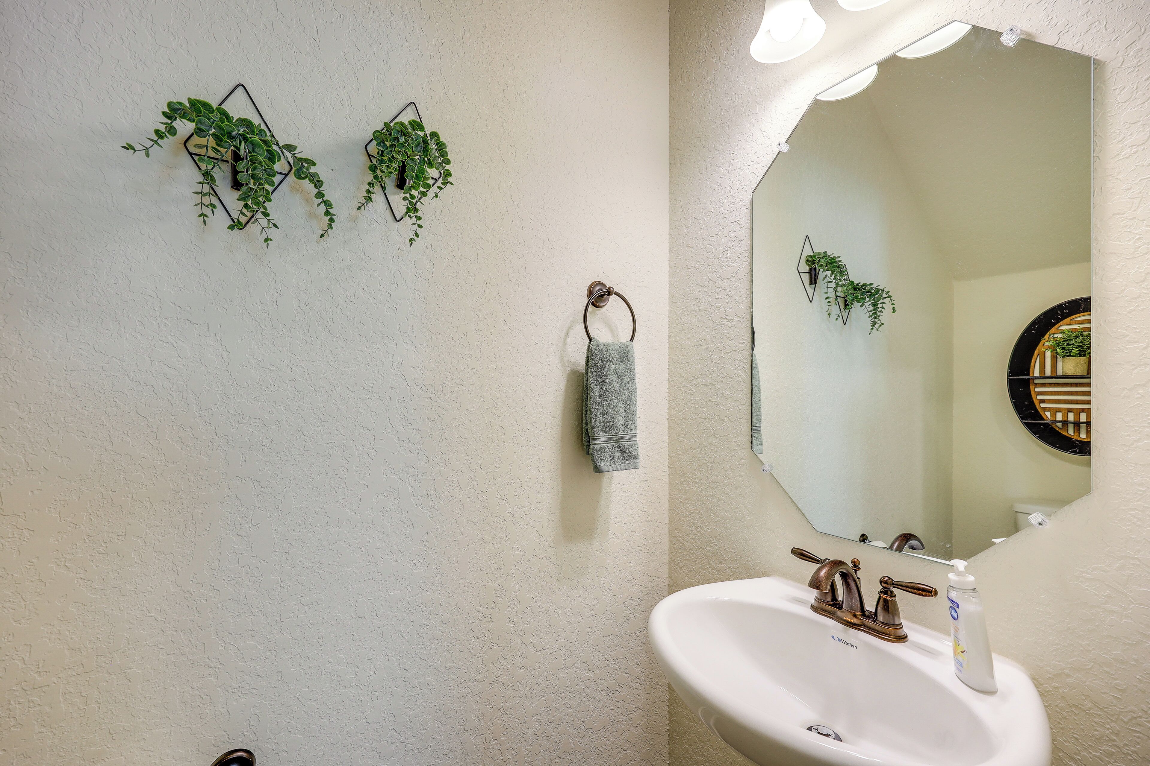Un baño con un lavabo blanco, un espejo iluminado y dos plantas colgantes.