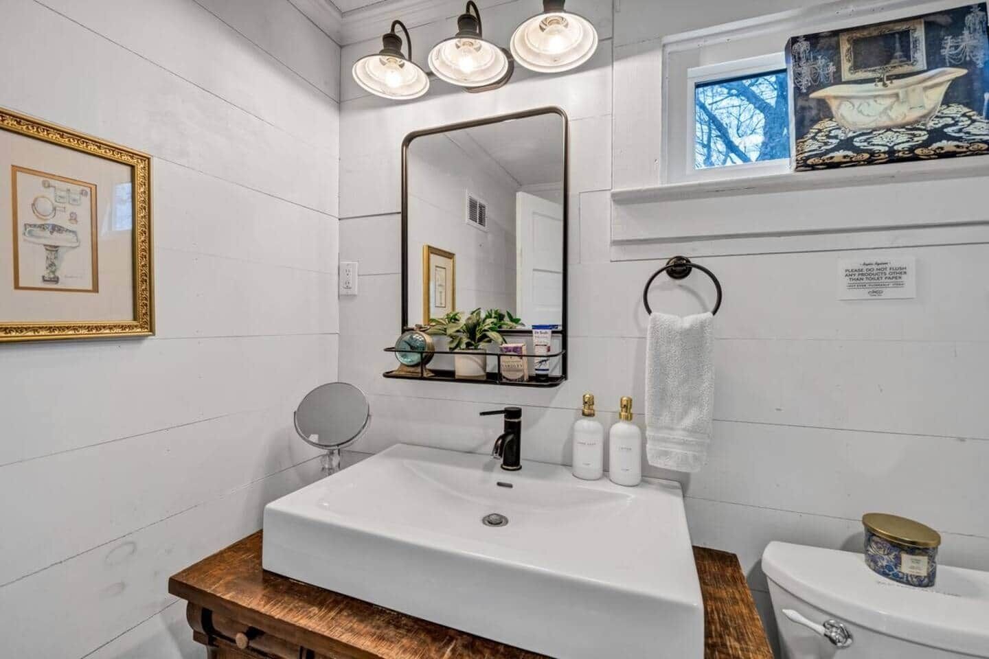 A bathroom with a white sink, a mirror, a toilet, and a shelf with toiletries.
