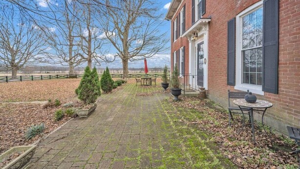 Un bâtiment en briques avec une cour dallée, des plantes en pot et une table entourée de chaises.