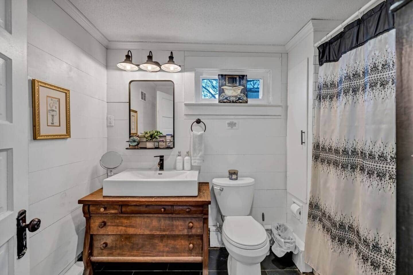 Un bany amb un moble de tocador de fusta, un lavabo blanc, un vàter i una cortina de bany amb dibuixos.