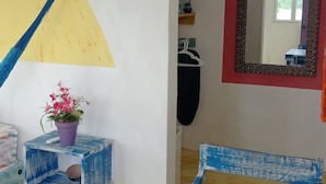 A room with a blue and yellow painted wall, a wooden table, a purple plant, and a mirror with a red frame. - Colorful room very close to the beach. Only one lot behind the best beach | 2 (Holbox Island)