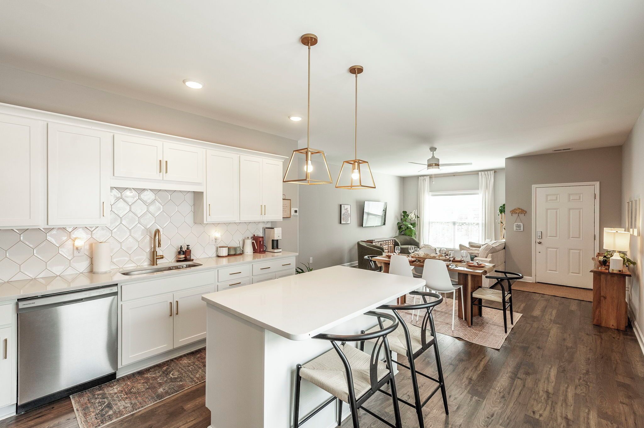 A modern kitchen with white cabinets, a stainless steel dishwasher, and a central island with bar stools.