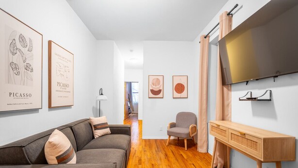 Een moderne woonkamer met een grijze bank, een houten salontafel en een aan de muur bevestigde televisie.
