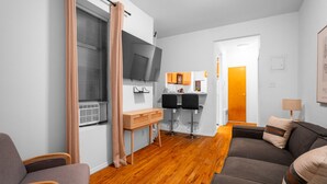 Een moderne woonkamer met een bank, een houten salontafel, een aan de muur bevestigde televisie, en een keukenhoek met een aanrecht en krukken.