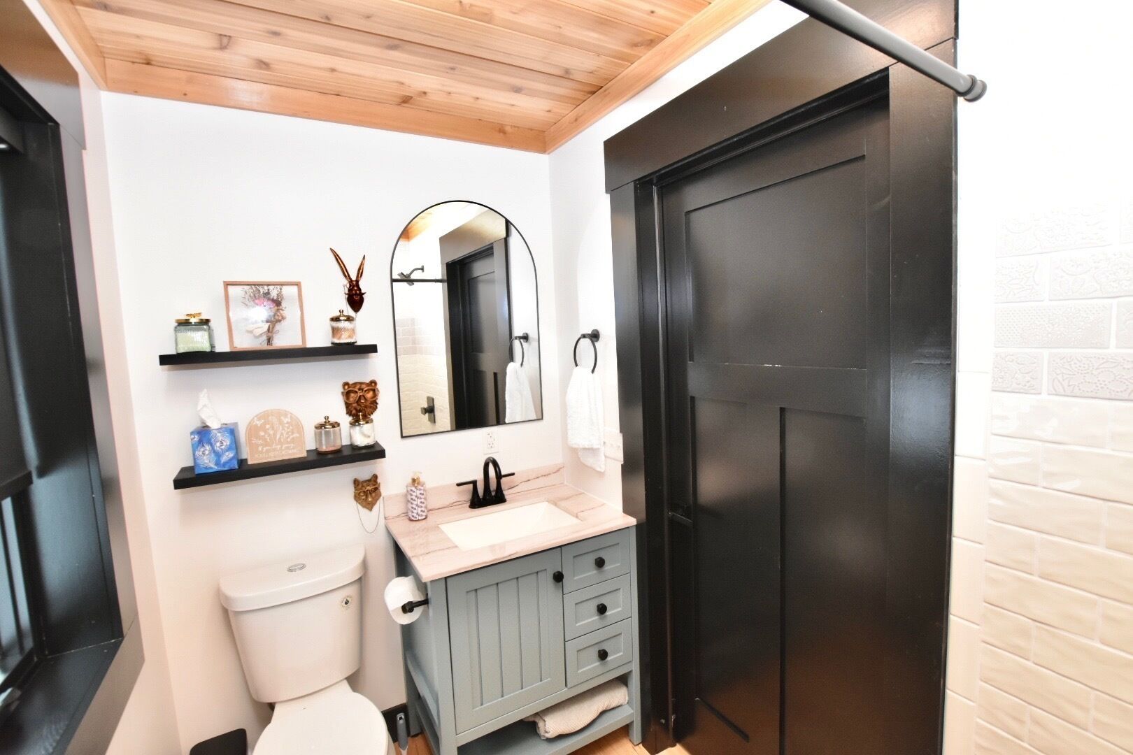 A bathroom with a toilet, sink, mirror, and a black door.