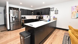 Una cocina moderna con armarios negros, un refrigerador de acero inoxidable, una isla blanca y una silla amarilla.