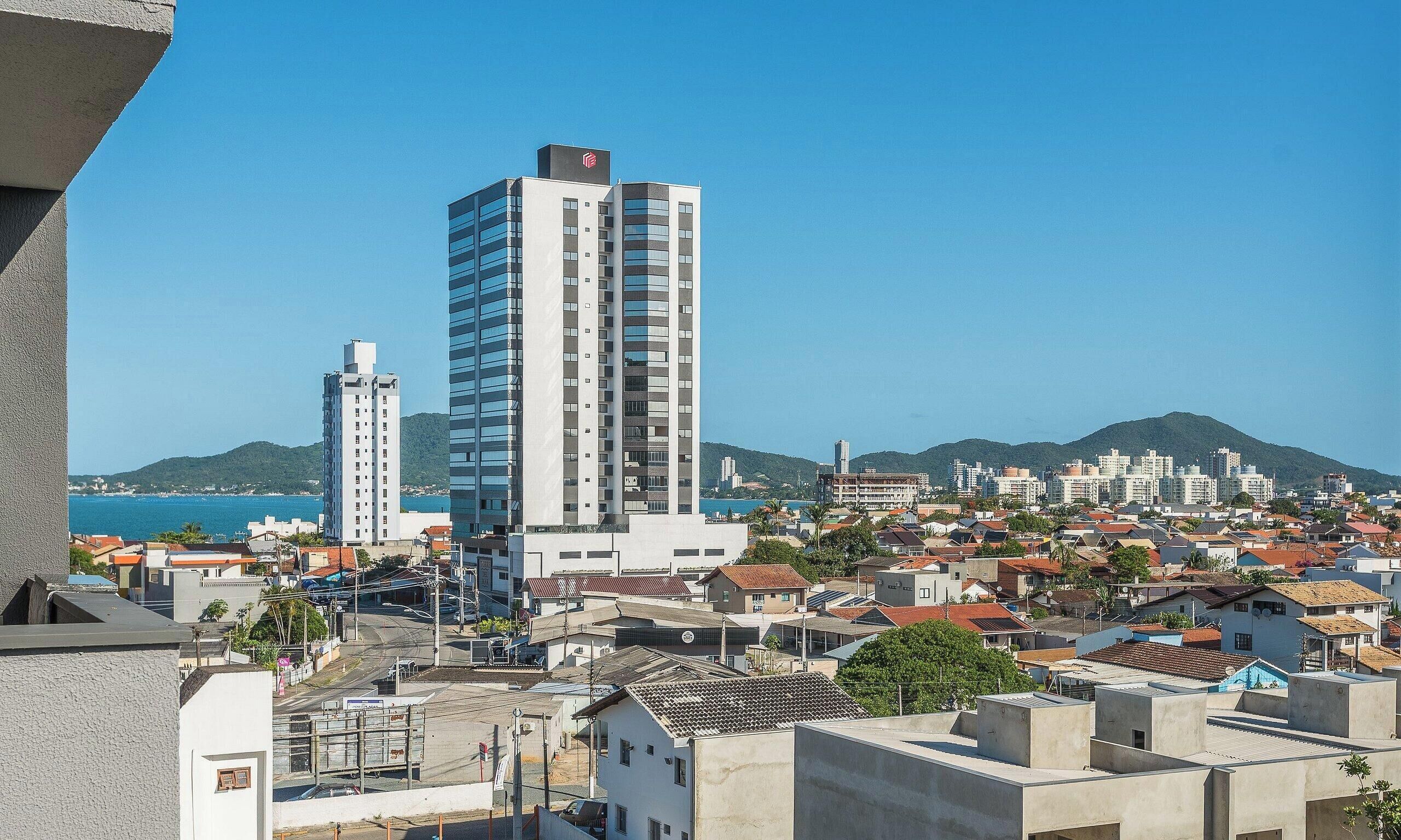 Un paisaje urbano costero con rascacielos, cielo despejado y montañas al fondo.