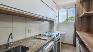 Eine Küche mit Granit Arbeitsplatte, Edelstahlspüle, weißen Schränken, einem Fenster und einem eingebauten Backofen.