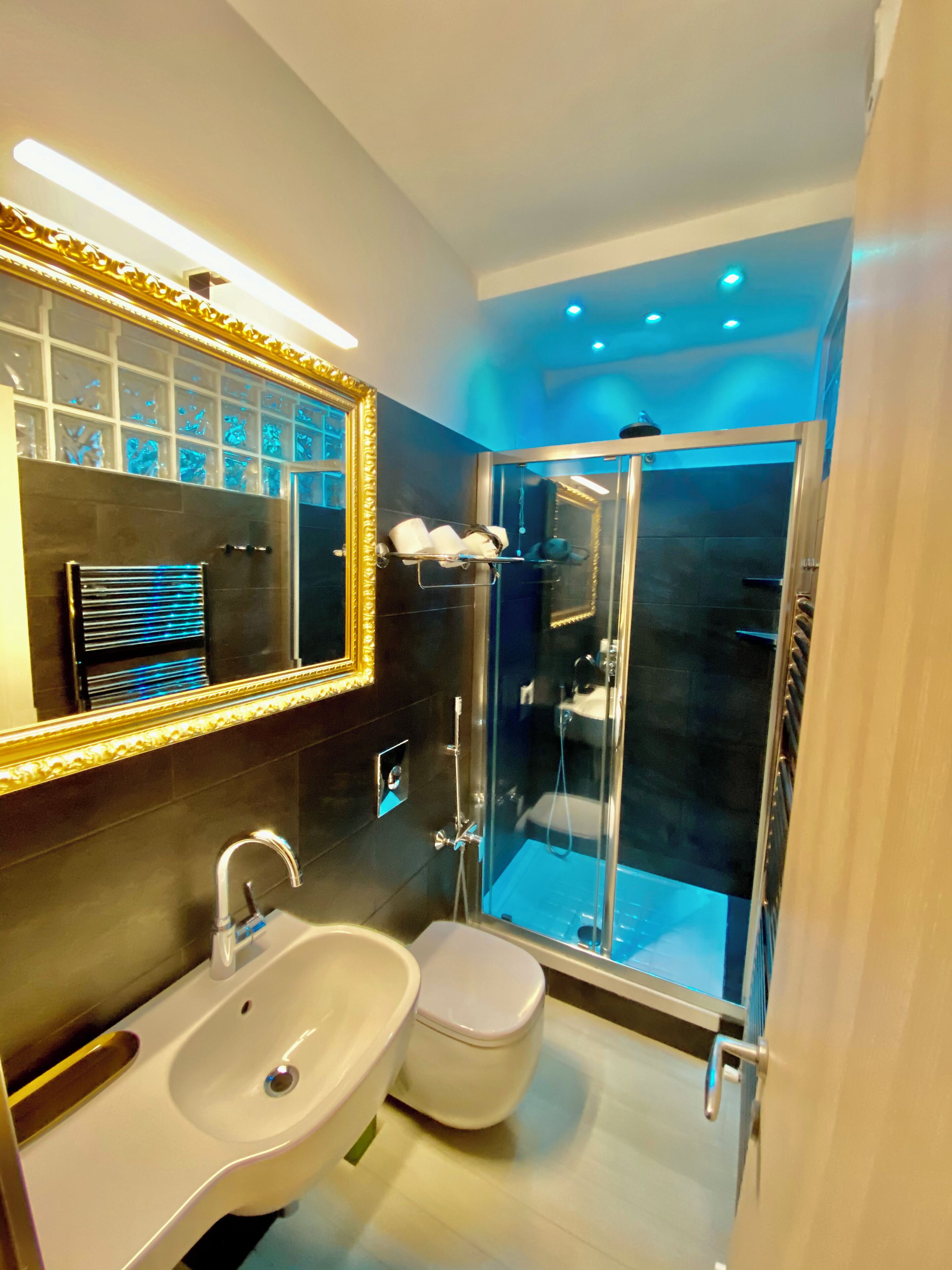 Une salle de bain moderne avec une douche à parois de verre, un lavabo blanc et un grand miroir avec un cadre doré.