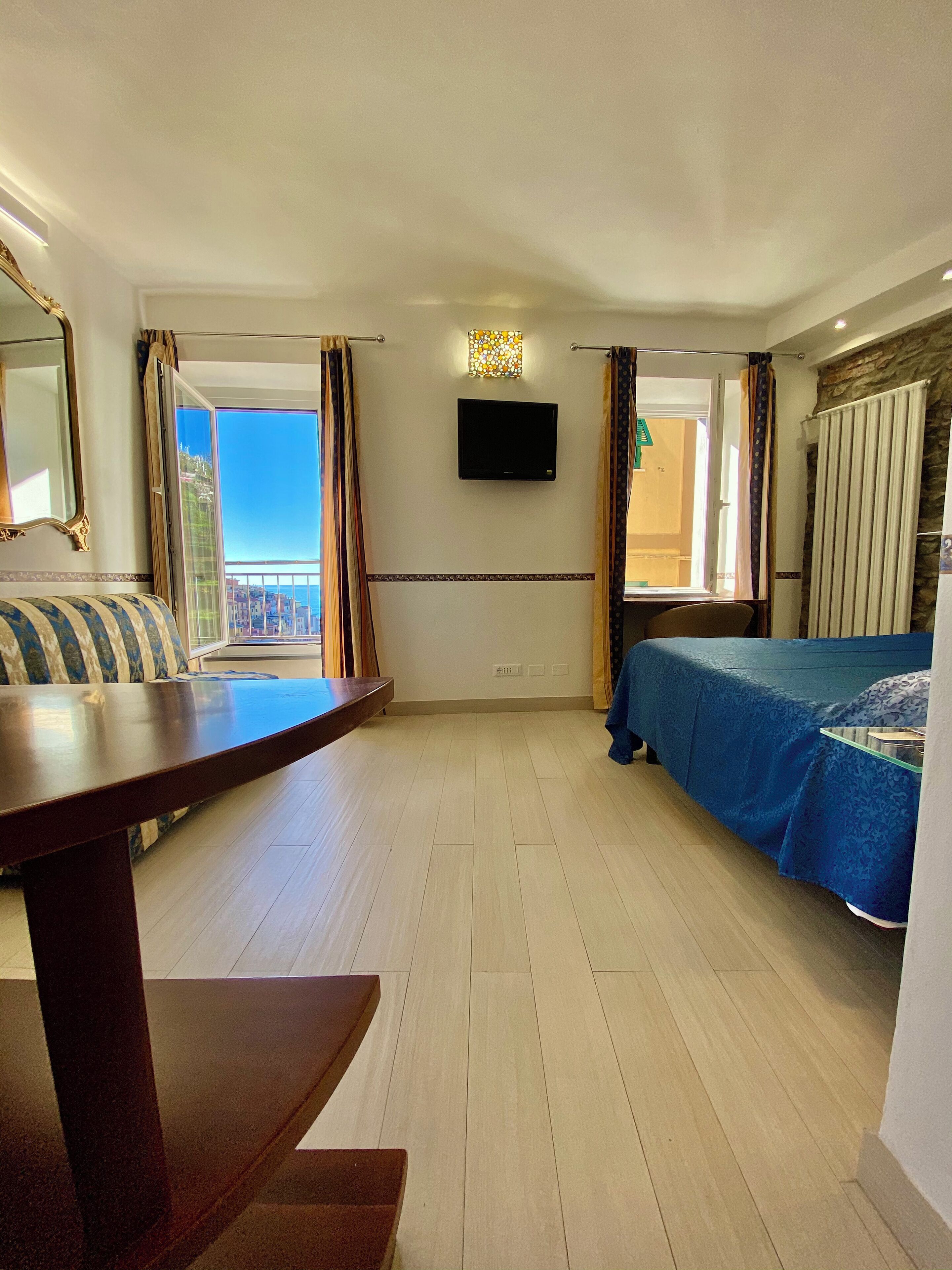 A hotel room with a balcony, a bed, a desk, and a TV.