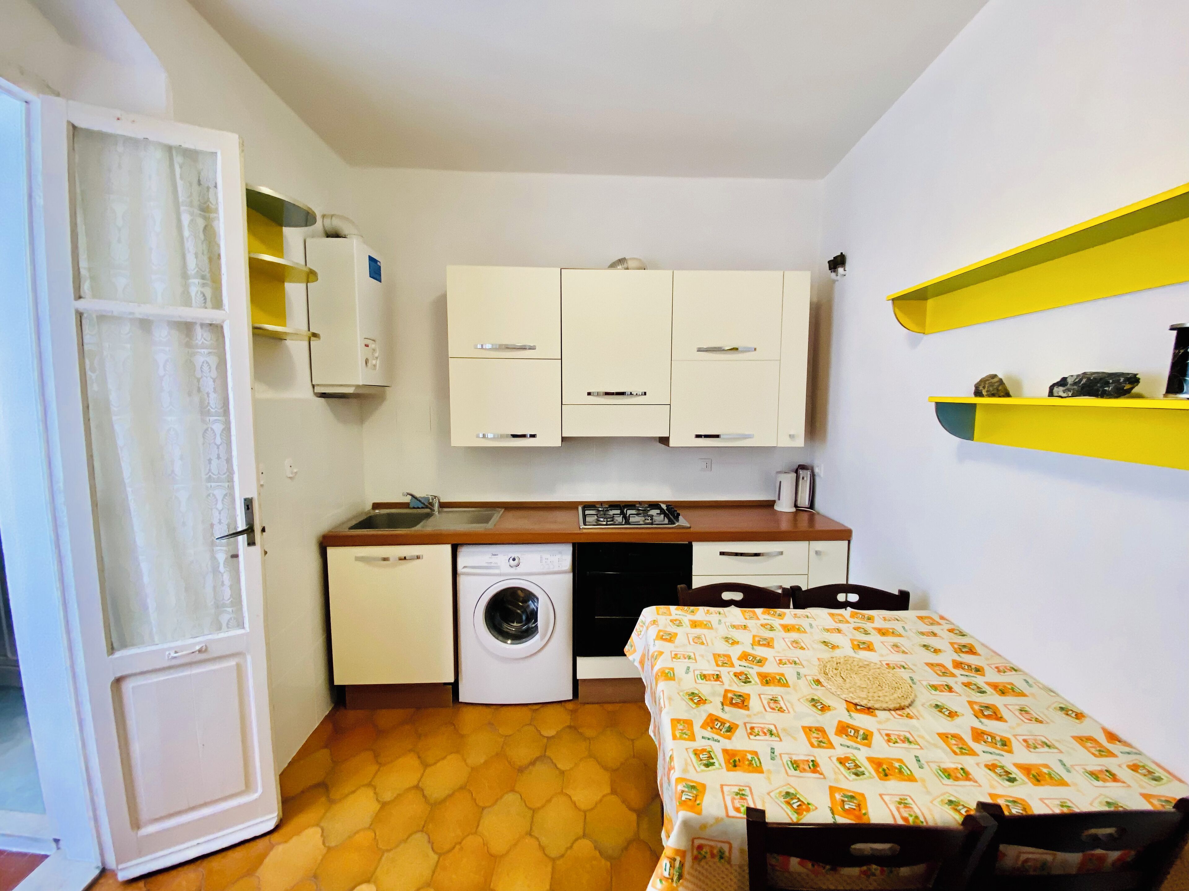 Una cocina funcional con lavadora, lavamanos y una mesa con mantel estampado.