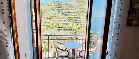An open door leading to a balcony with a table and chairs, a view of a hillside, and a tiled floor.