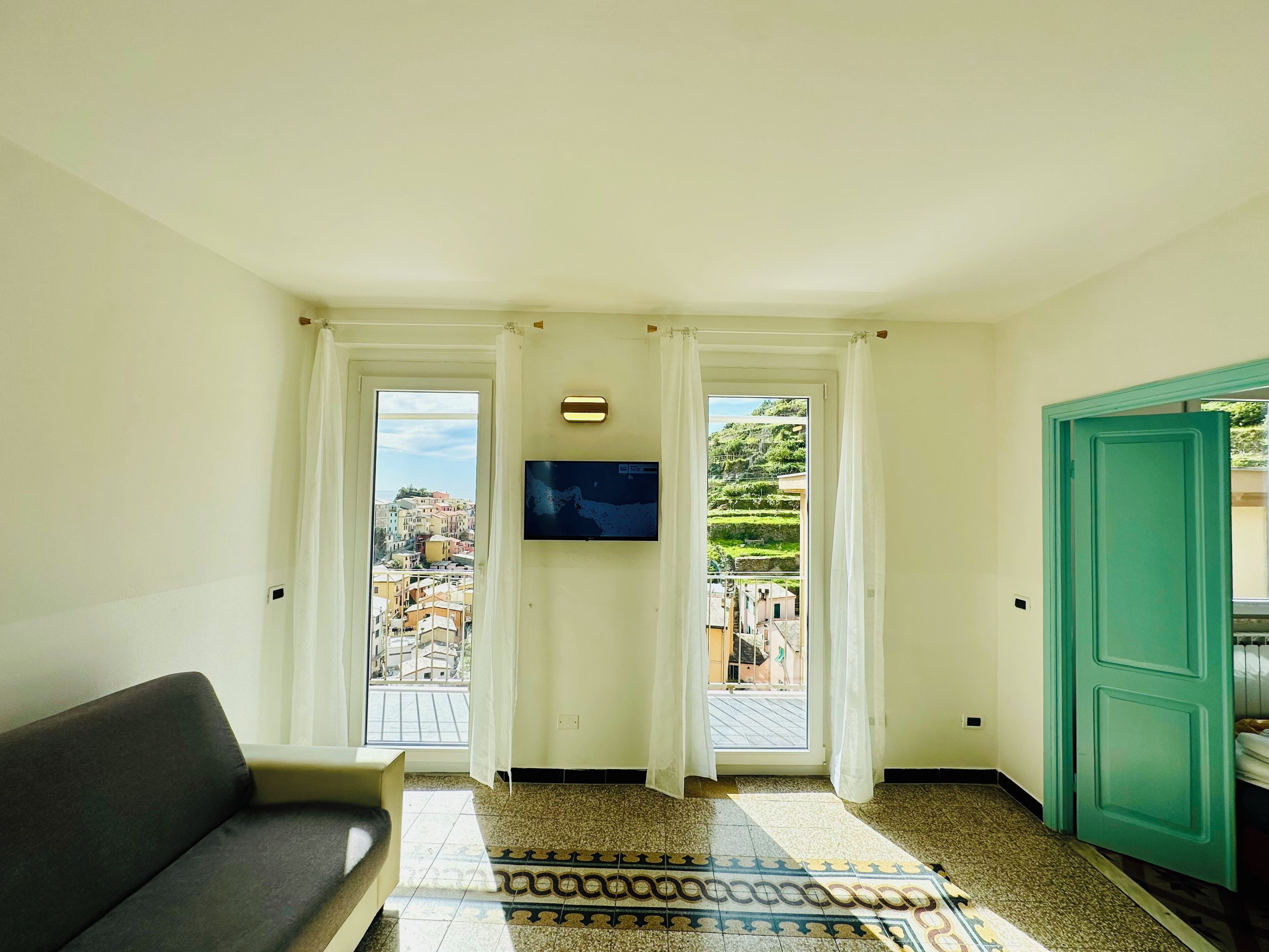 A room with a sofa, a patterned rug, a television, and two doors leading to balconies with city views.