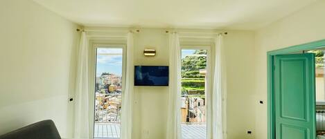 A room with a sofa, a patterned rug, a television, and two doors leading to balconies with city views.