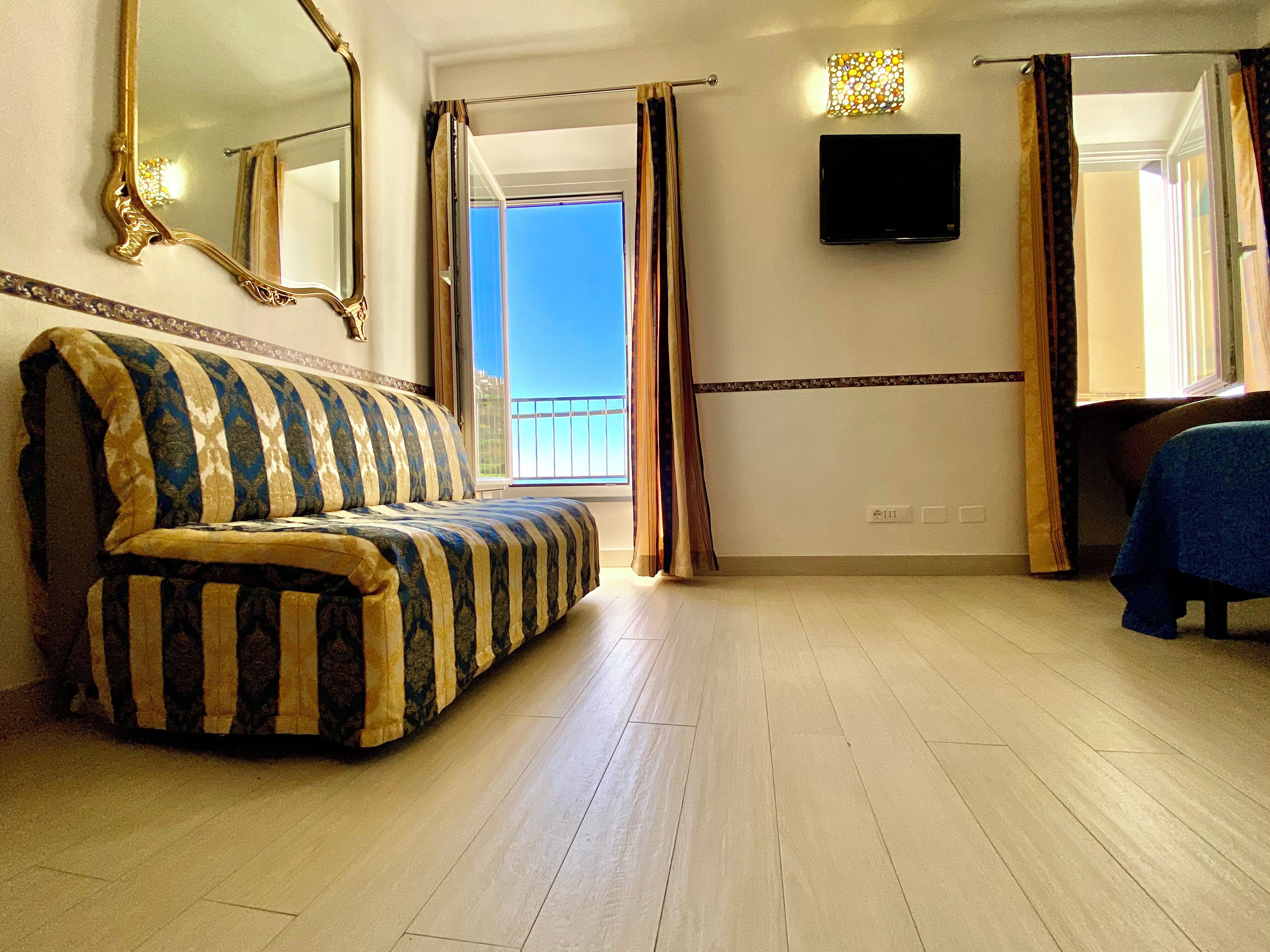 Une chambre d’hôtel avec un canapé à motifs, une télévision et un balcon avec des rideaux.