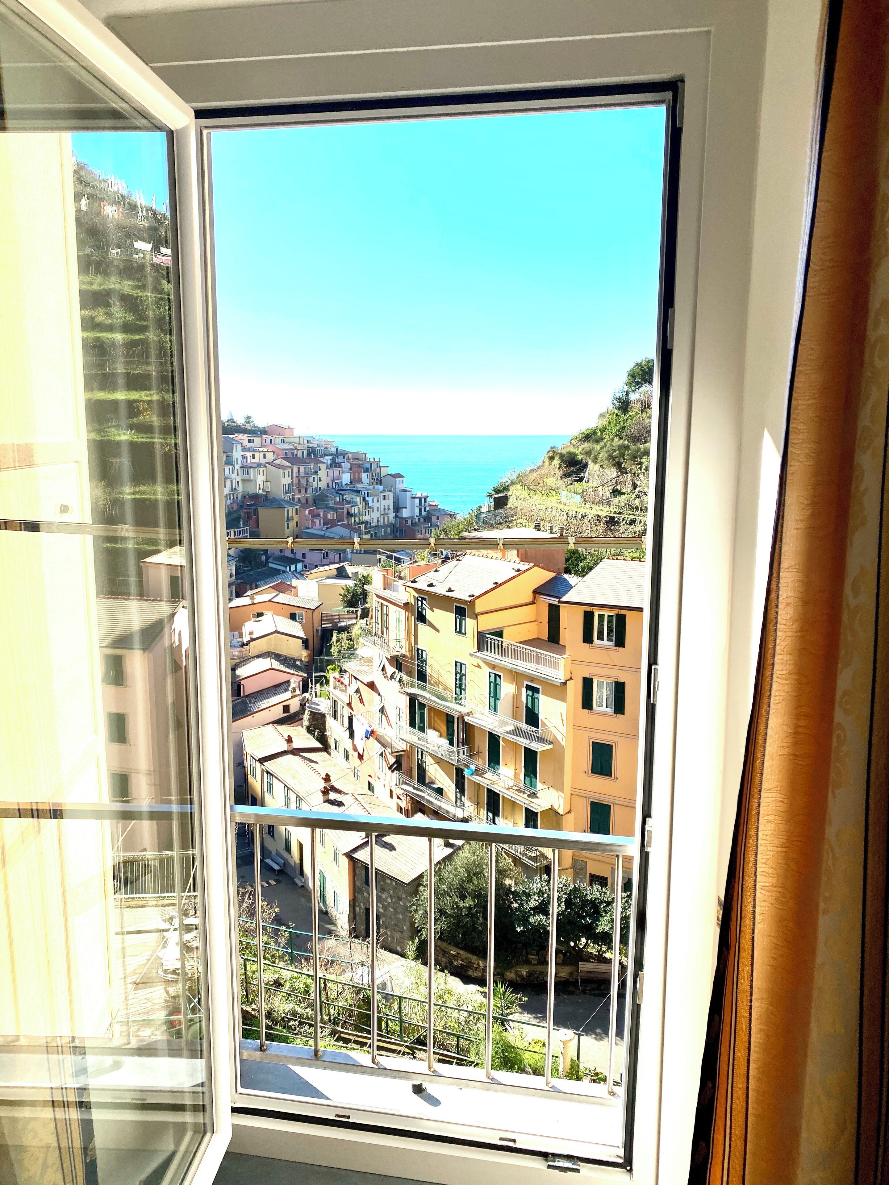 Une vue depuis une fenêtre donnant sur une ville côtière, avec ses bâtiments et un ciel bleu dégagé.