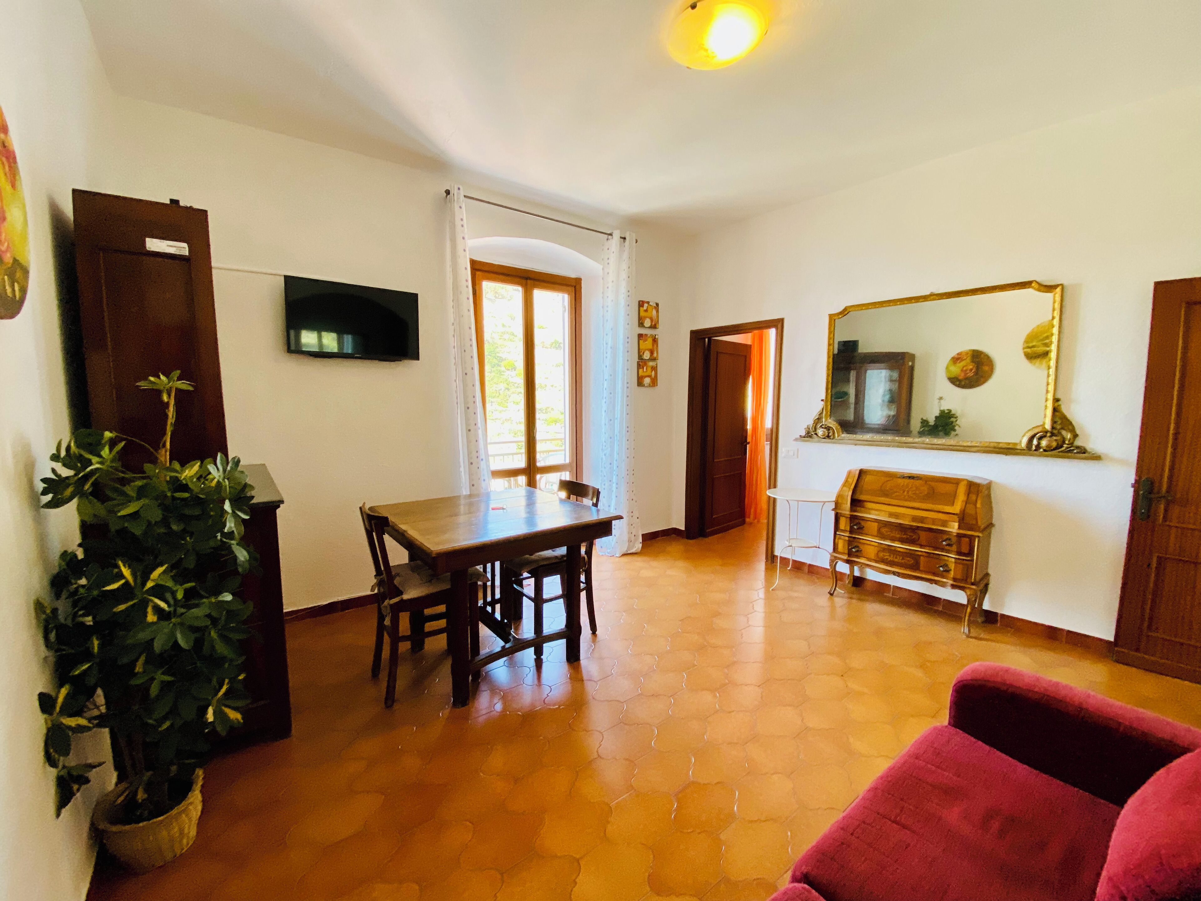 Una sala de estar con una mesa de comedor de madera, sillas, un sofá rojo, un televisor y un espejo en la pared.