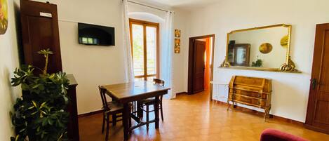 Una sala de estar con una mesa de comedor de madera, sillas, un sofá rojo, un televisor y un espejo en la pared.