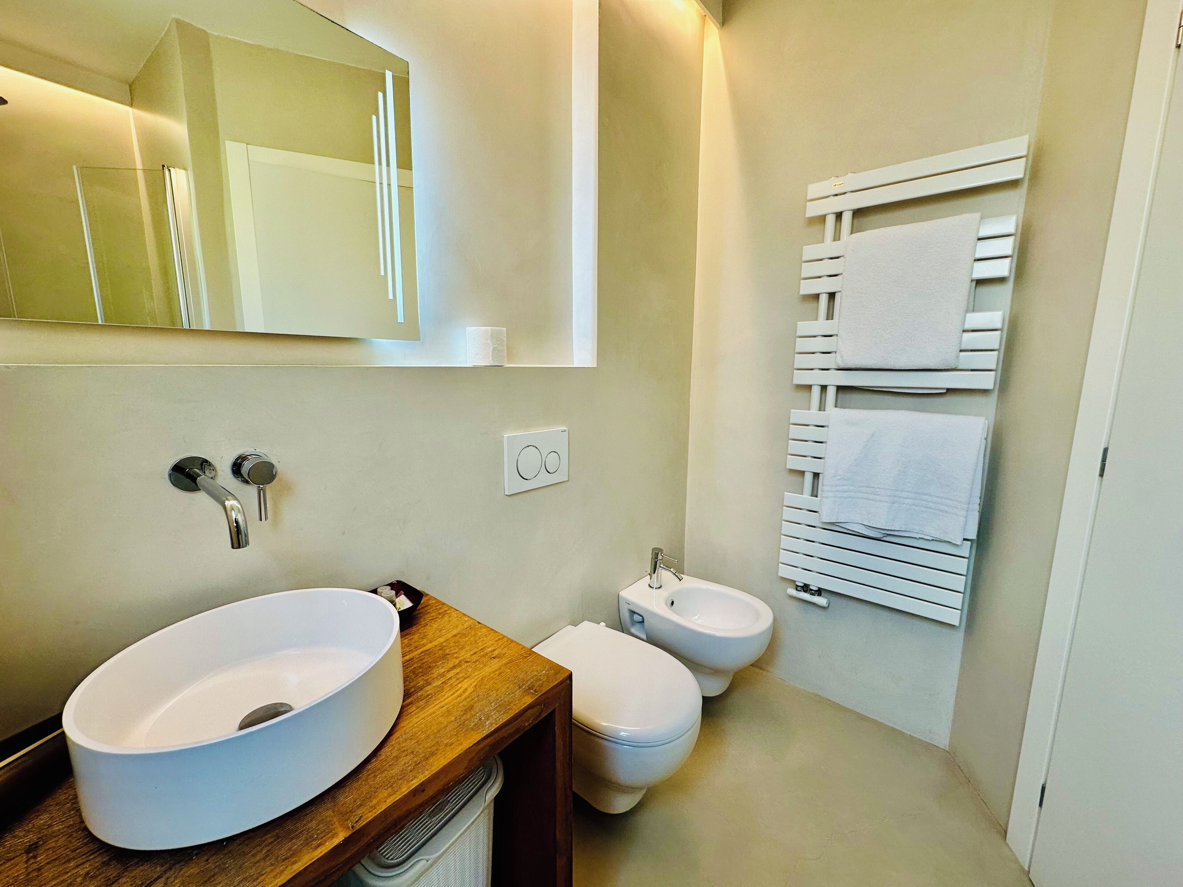 A bathroom with a wooden vanity, a white sink, a bidet, and a towel rack.