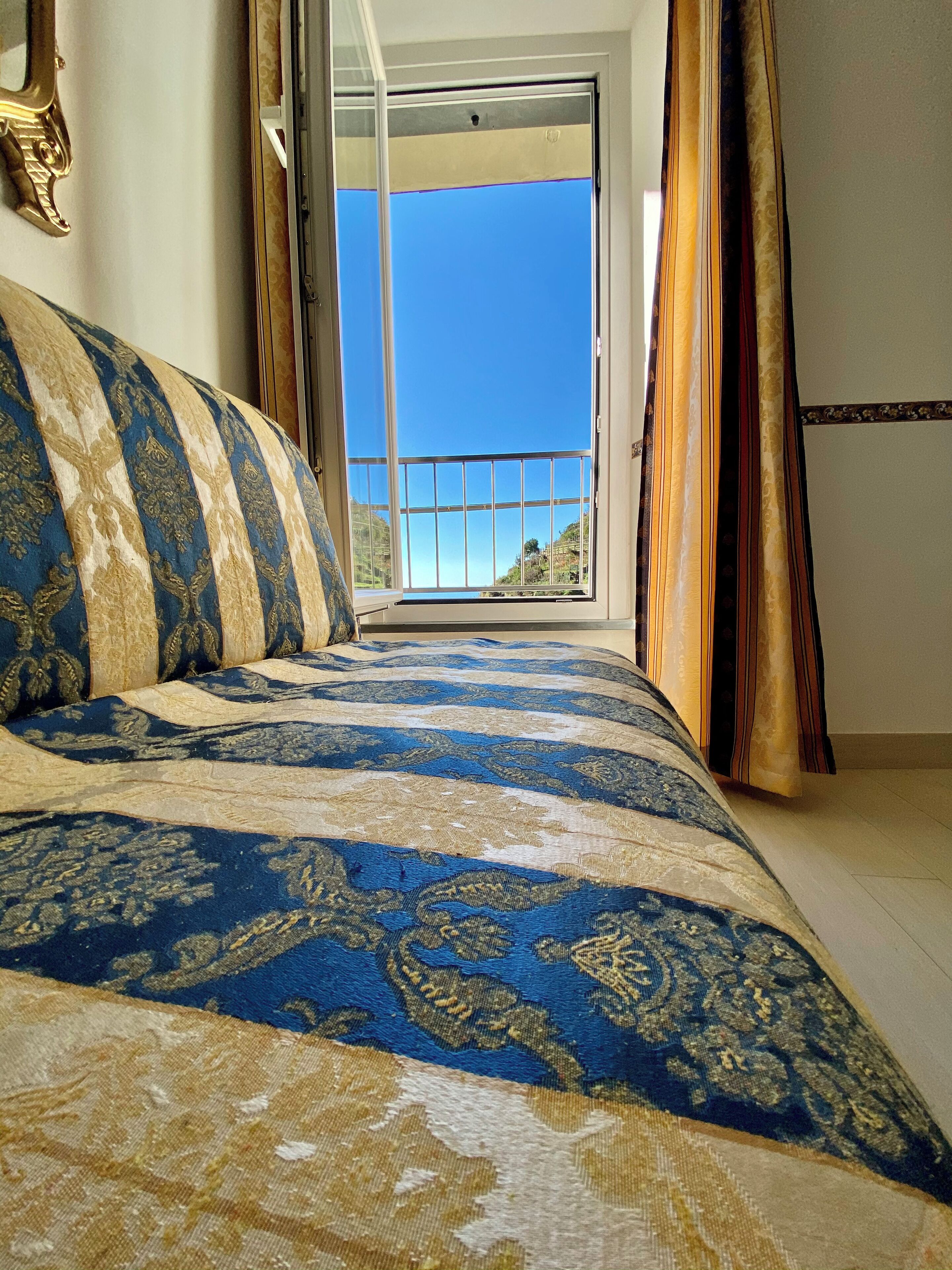 Ein Schlafzimmer mit einem großen Bett, Blick ins Freie durch eine Schiebetür und einem Balkon mit Geländer.