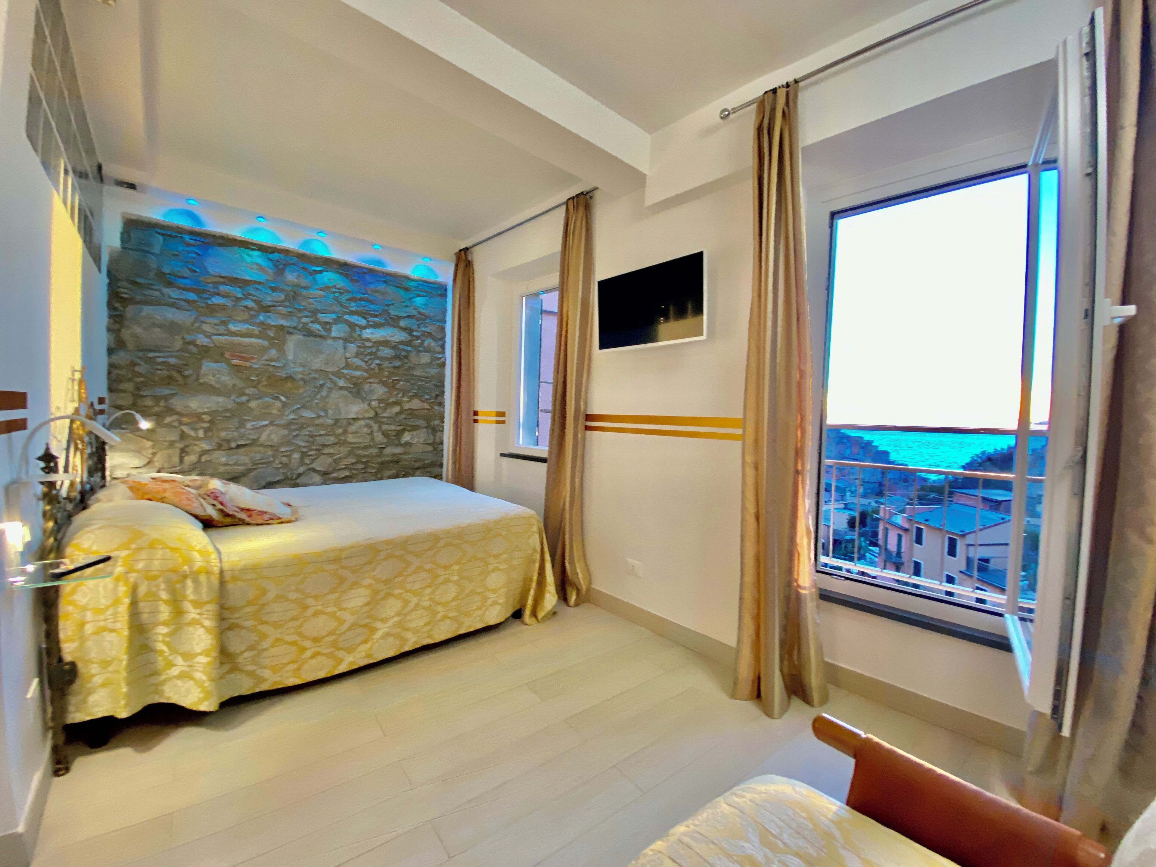 A bedroom with a bed, a stone wall, a TV, and a window with a view.