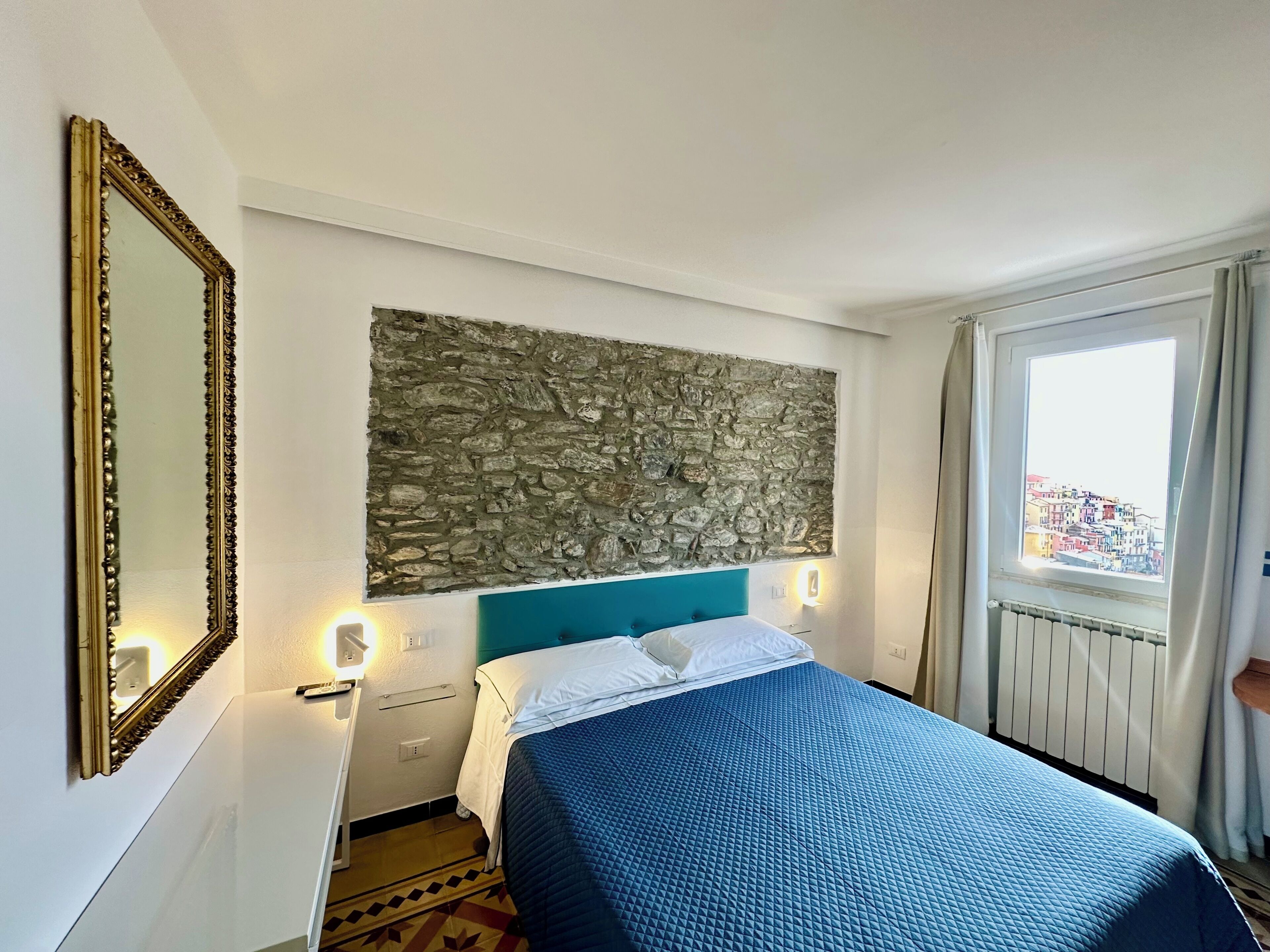 Una habitación de hotel con cama, pared de piedra, ventana con vistas y espejo.