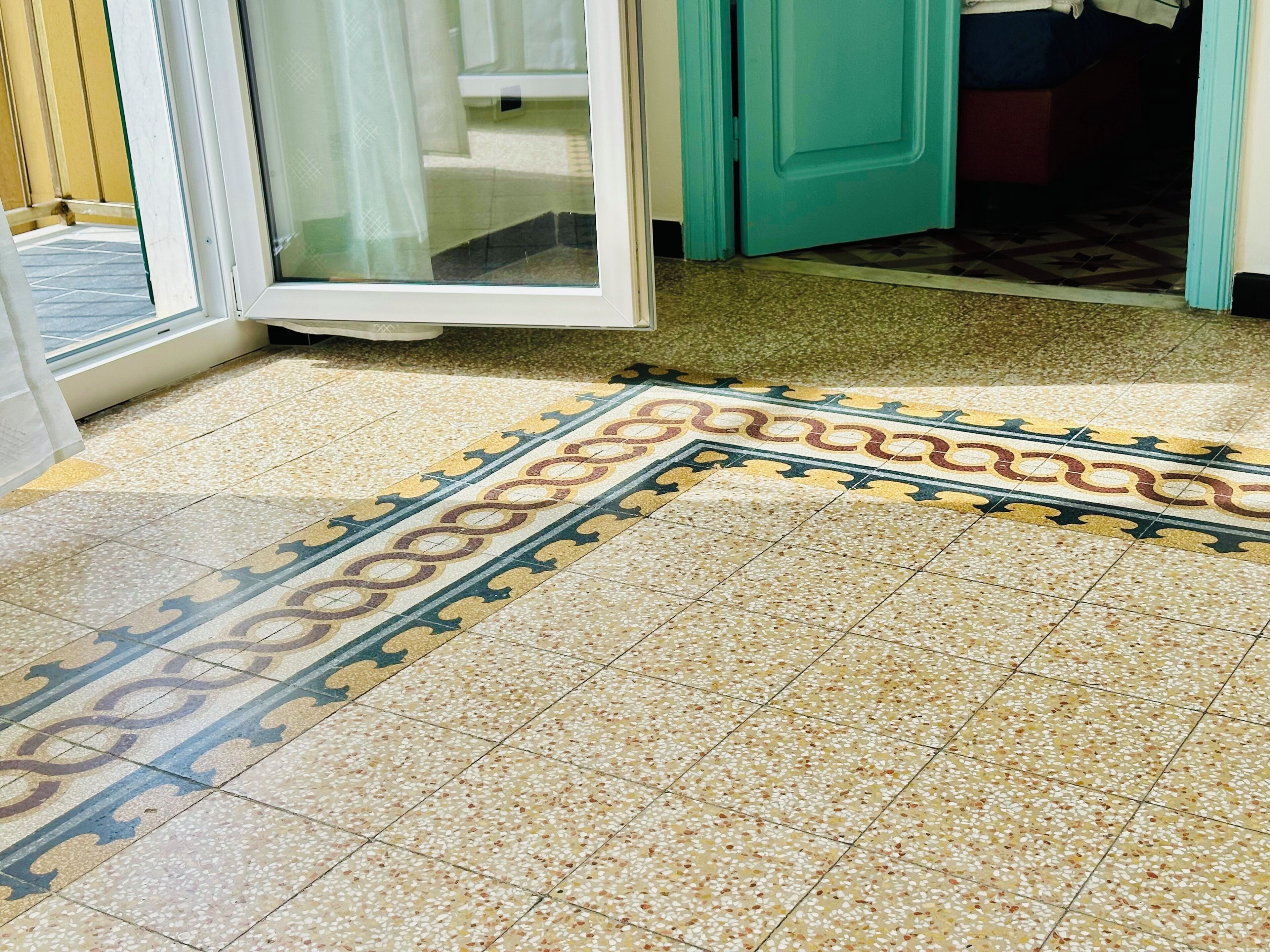 A tiled floor with a decorative border and a door leading to a room.