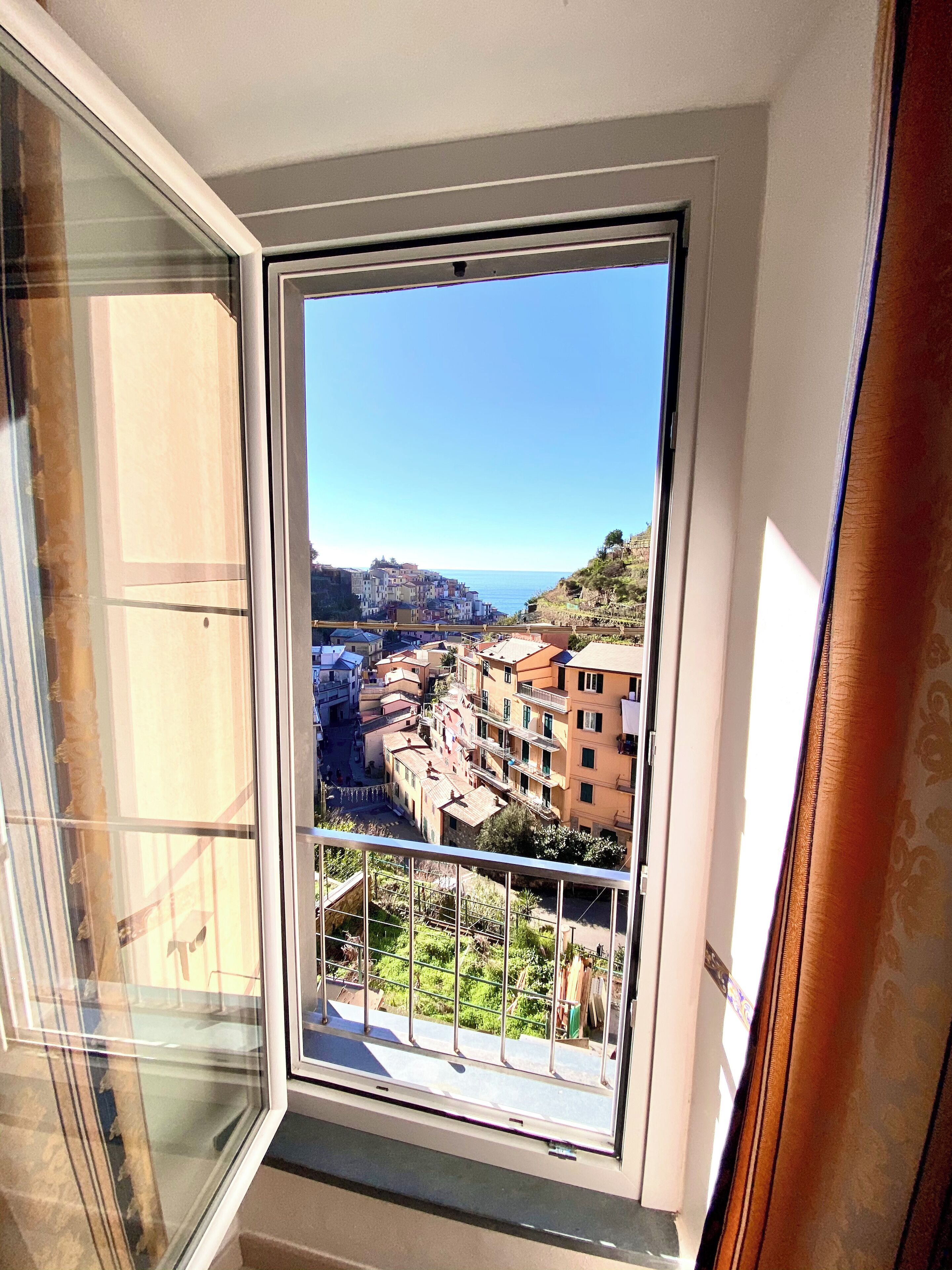 A balcony with a metal railing overlooking a coastal town with buildings and a clear sky.