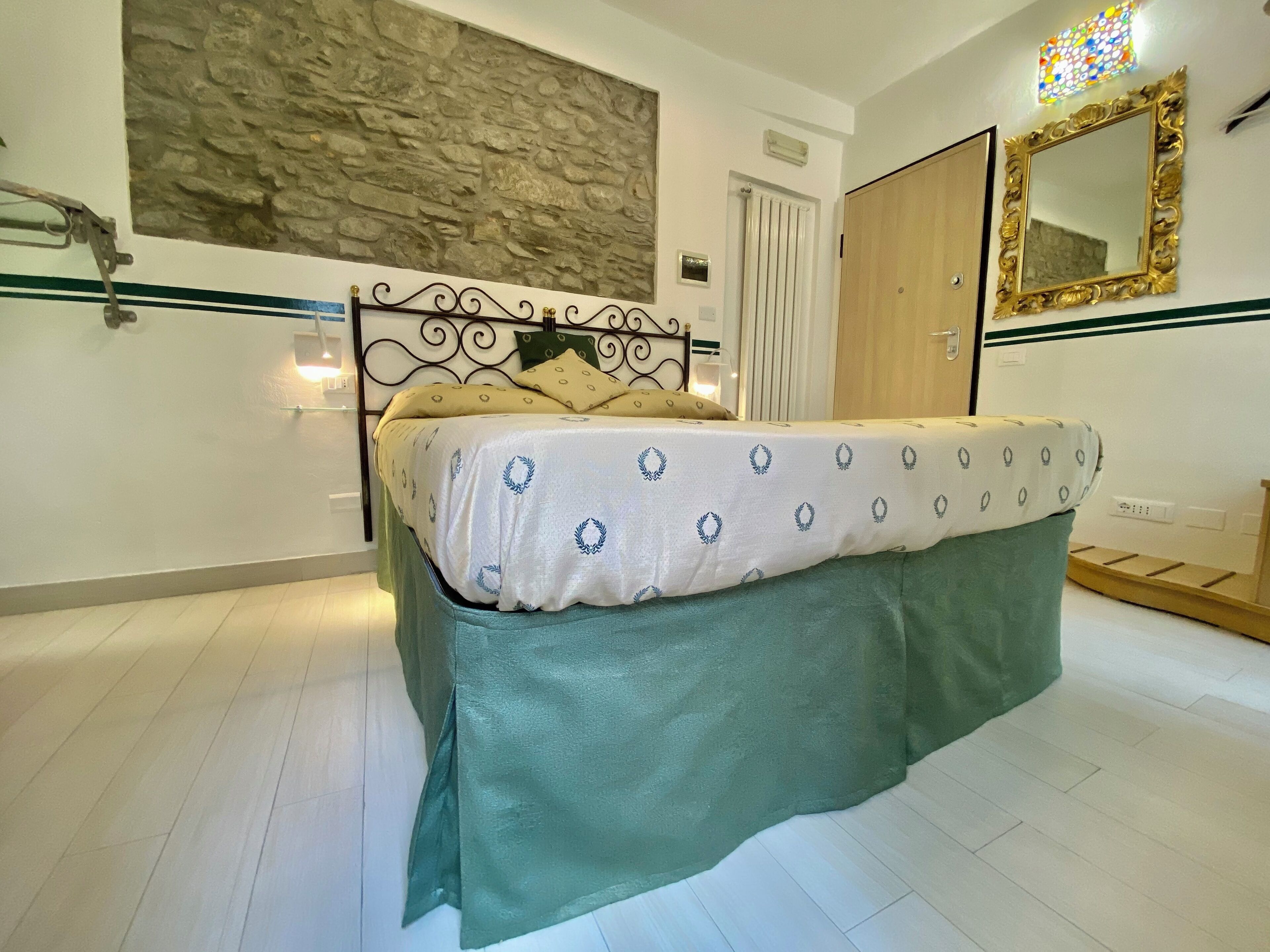 A bedroom with a bed, a stone wall, a wooden door, a mirror, and a radiator.
