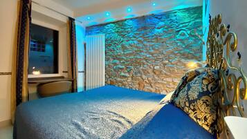 A bedroom with a stone wall, a bed with a patterned headboard, and a window with curtains.