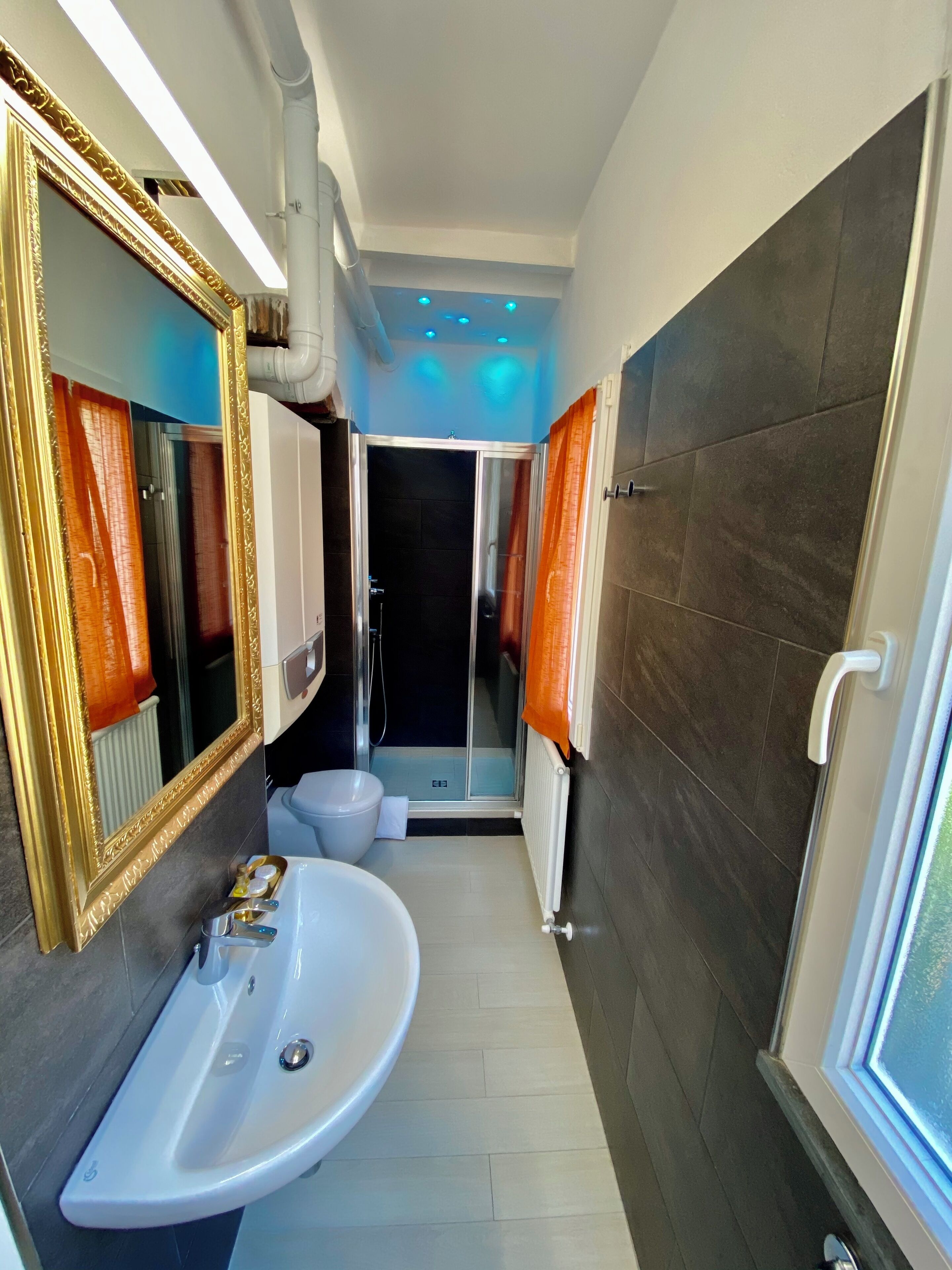 Un bagno moderno con un ampio specchio, lavandino bianco e pareti rivestite di piastrelle scure.