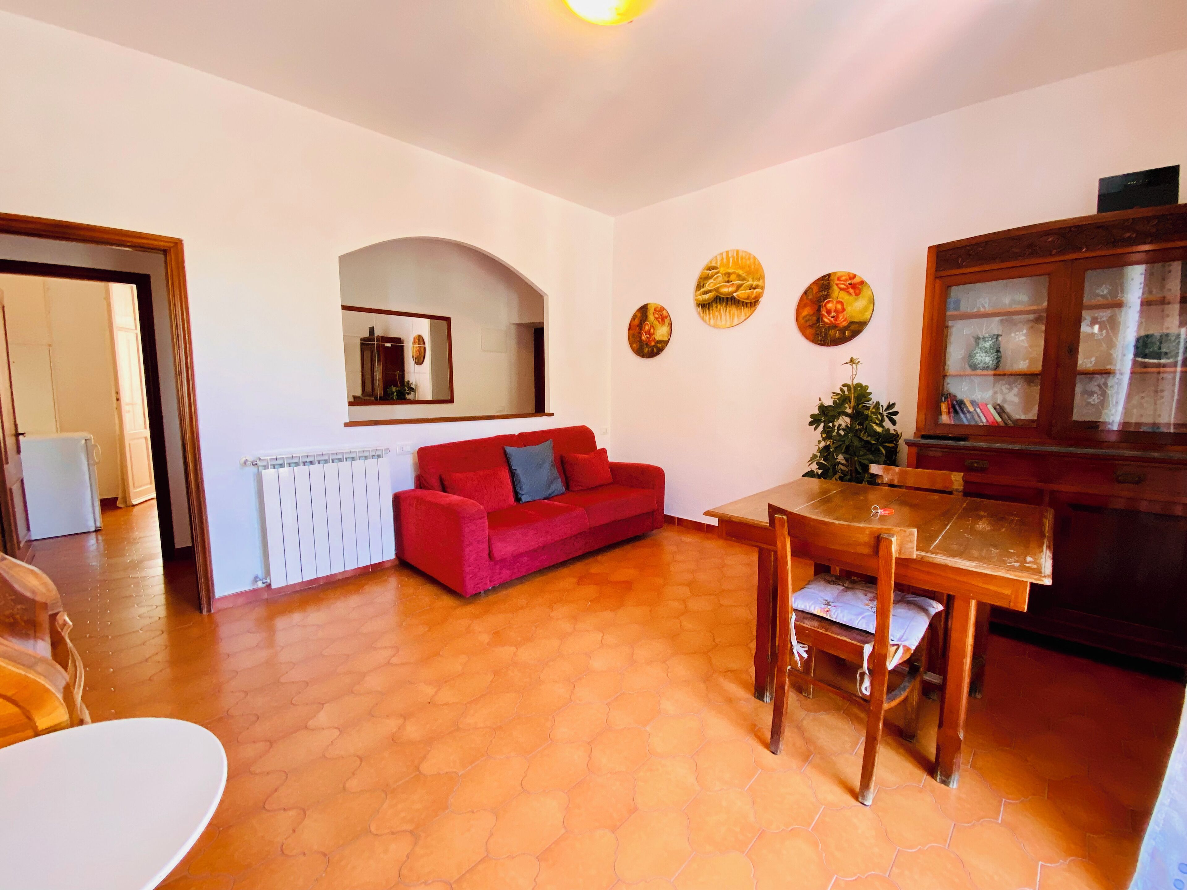 A living room with a red sofa, a wooden dining table, and a cabinet with glass doors.